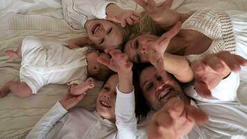 alegre família do cinco pessoas estão deitado em a cama, rindo e acenando seus mãos. Visão a partir de acima. video
