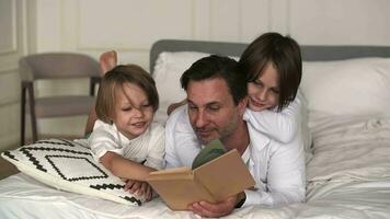 A father reads a book to his sons while lying on his bed. video