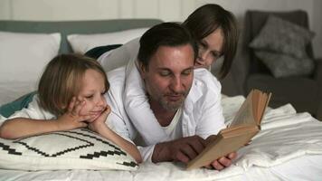 A father reads a book to his sons while lying on his bed. video