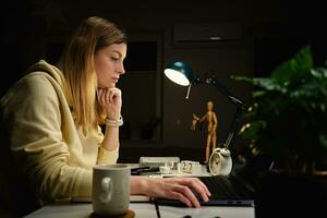 Woman works at home office at night, using laptop photo