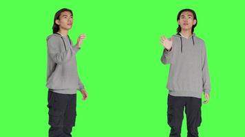 Young adult checking hologram icon in studio with greenscreen backdrop, looking at modern holographic image and focusing on work. Asian casual guy using artificial intelligence. video