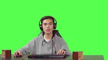 POV of guy playing online games at pc while he enjoys gameplay with his friends, using headphones at his desk. Asian gamer having fun with action game at workstation, greenscreen backdrop. video