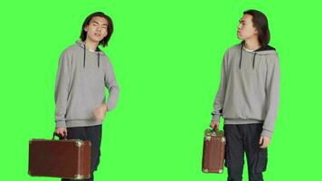 Male model waiting in studio, looking around and checking time on wristwatch. Person carrying vintage suitcase standing over greenscreen backdrop, acting impatient on camera. video