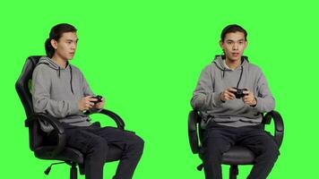 Asian guy playing videogames over greenscreen backdrop, using controller and having fun with friends on online gaming competition. Young man gamer enjoying rpg gameplay, blank background. video