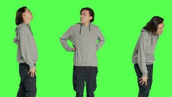 Male model suffering from back pain in studio, dealing with lower spine cramps while he is standing over greenscreen. Young adult being in pain and suffering from spinal pressure, backache. video