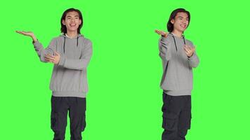 Asian man presenting marketing ad over greenscreen backdrop, creating advertisement for new promotion. Male model pointing at something on both sides of the studio, commercial. video