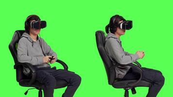 Player having fun with vr headgear and controller, playing online gaming contest with other people. Asian person enjoying leisure activity while he sits on chair against greenscreen backdrop. video