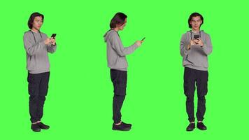 Adult texting messages on phone standing over greenscreen background, using social media app to chat remotely with friends. Asian joyful person messaging on modern smartphone. video