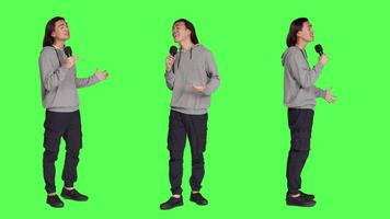 Cool adult doing karaoke session in studio, using microphone to sing trendy tunes and lyrics. Young person having fun over full body greenscreen backdrop, creating music and singing songs. video