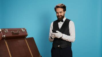 Doorkeeper browses social media app on camera, using smartphone to text messages or review list of online reservations. Professional hotel porter texting on mobile phone, studio shot. photo