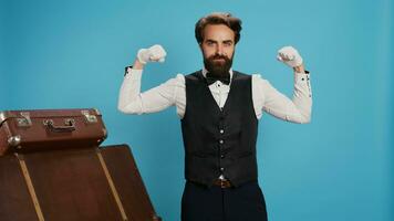 Modern bellboy flexing muscles in studio, showing off strength underneath his formal uniform attire. Hotel porter doorman feeling powerful on camera, showing determination in hospitality industry. photo