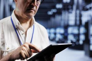 Octogenarian empoyee inspects operational blade servers in computer network security data center, ensuring flawless performance. Proficient worker monitoring energy consumption across equipment parts photo