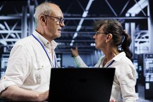 Aged professionals preventing strain on server farm systems caused by AI applications driving up power usage. Adept servicemen maintenancing supercomputers doing intense computations photo