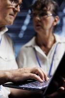 Octogenarian IT developers running analysis on server rows helping businesses manage databases, host websites and store files. Licensed programmers auditing high tech data center gadgets photo