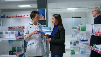 Healthcare specialist in apothecary with patient prescribing her melationin pills to cure sleeping issues. Asian customer receiving insomnia medical product from chemist store worker photo