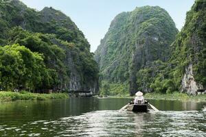 Activity downstream on boat with vietnamese using foot paddle and view limestone mountain in Ngo Dong river photo