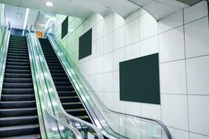 Public escalator with blank billboard on wall photo