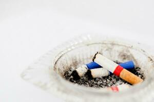 Close-up of cigarette butt in ashtray. Glass cigarette ashtray on white background. Concept of health and dangers of smoking. photo