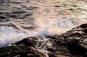 the ocean waves crashing against the rocks at sunset photo