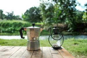 Vintage electric lantern and glass dripper carafe on a folding table for camping at river side blur background photo