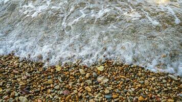Close up soft wave lapped the gravel beach. Beautiful sea waves with foam. Abstract texture background. photo