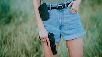 A girl in denim shorts and with a pistol in her hand poses for a photo.. Close-up photo