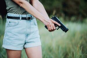 A girl in denim shorts and with a pistol in her hand poses for a photo.. Close-up photo