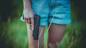 A girl in denim shorts and with a pistol in her hand poses for a photo.. Close-up photo