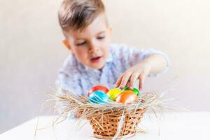 Little boy takes an Easter egg from a basket from the table on a white background. photo