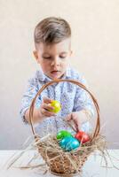 Little boy lays a yellow easter egg in a basket from the table on a white background. photo