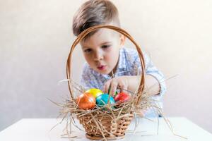 Little boy takes an Easter egg from a basket from the table on a white background. photo