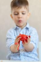 A boy holds a red Easter egg in his hands stained with paint on a white background. photo