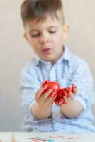 A boy holds a red Easter egg in his hands stained with paint on a white background. photo