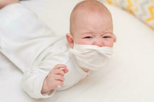 pequeño bebé en un médico máscara mentiras en cuarentena a hogar durante el coronavirus y covid-19 pandemia. foto