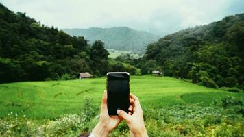 View over the mobile phone display during shoot. Holding the mobile phone in hands and taking a photo, focused on mobile phone screen. Delightful mountain landscape and blue sky. photo