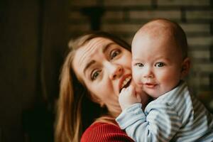 A mother holds a baby in her arms. Mom hugs her toddler. Girl has fun and rejoices with the child. A woman clutches a infant. photo