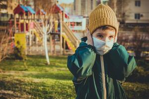 A child in a medical mask stands near the playground during the pandemic of coronavirus and Covid - 19 photo