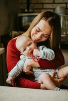 un madre sostiene un bebé en su brazos. mamá abrazos su niño pequeño. niña tiene divertido y se regocija con el niño. un mujer garras un niño. foto