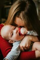 A mother holds a baby in her arms. A mom kisses a infant. A women hugs her toddler. A girl has fun and rejoices with the child. photo