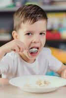 Beautiful boy eats milk porridge. Cute baby having breakfast sitting at a table in the kitchen at home. photo