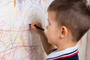 Boy draws on the wall with colored chalk. The child is engaged in creativity at home photo