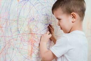 Boy draws on the wall with colored chalk. The child is engaged in creativity at home photo