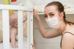 Prevention of the epidemic of coronavirus and covid-19. A mother in a protective mask looks after a baby who is in quarantine at home photo