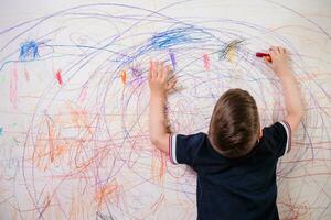 el niño sorteos en el pared con un lápiz de color. el chico es comprometido en creatividad a hogar foto