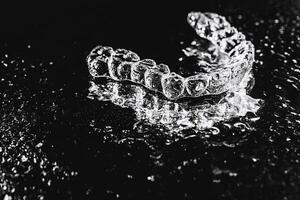 Transparent aligners, tooth retainers lie on a mirror with water droplets on a black background photo