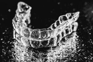 Transparent aligners, tooth retainers lie on a mirror with water droplets on a black background photo