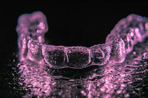 Transparent aligners, tooth retainers lie on a mirror with water droplets on a black background photo