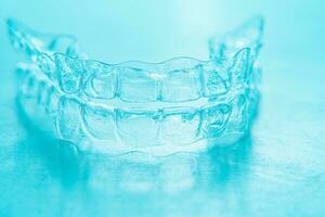 Invisible dental teeth brackets tooth aligners on turquoise background. Plastic braces dentistry retainers to straighten teeth. photo