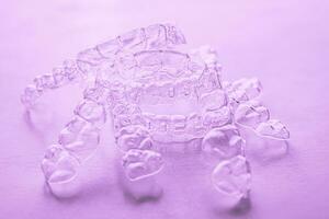 Invisible dental teeth brackets tooth aligners on pink background. Plastic braces dentistry retainers to straighten teeth. photo