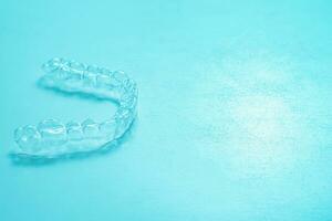 Invisible dental teeth brackets tooth aligners on turquoise background. Plastic braces dentistry retainers to straighten teeth. photo